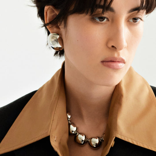 Large metallic stud earrings worn by model with short dark hair