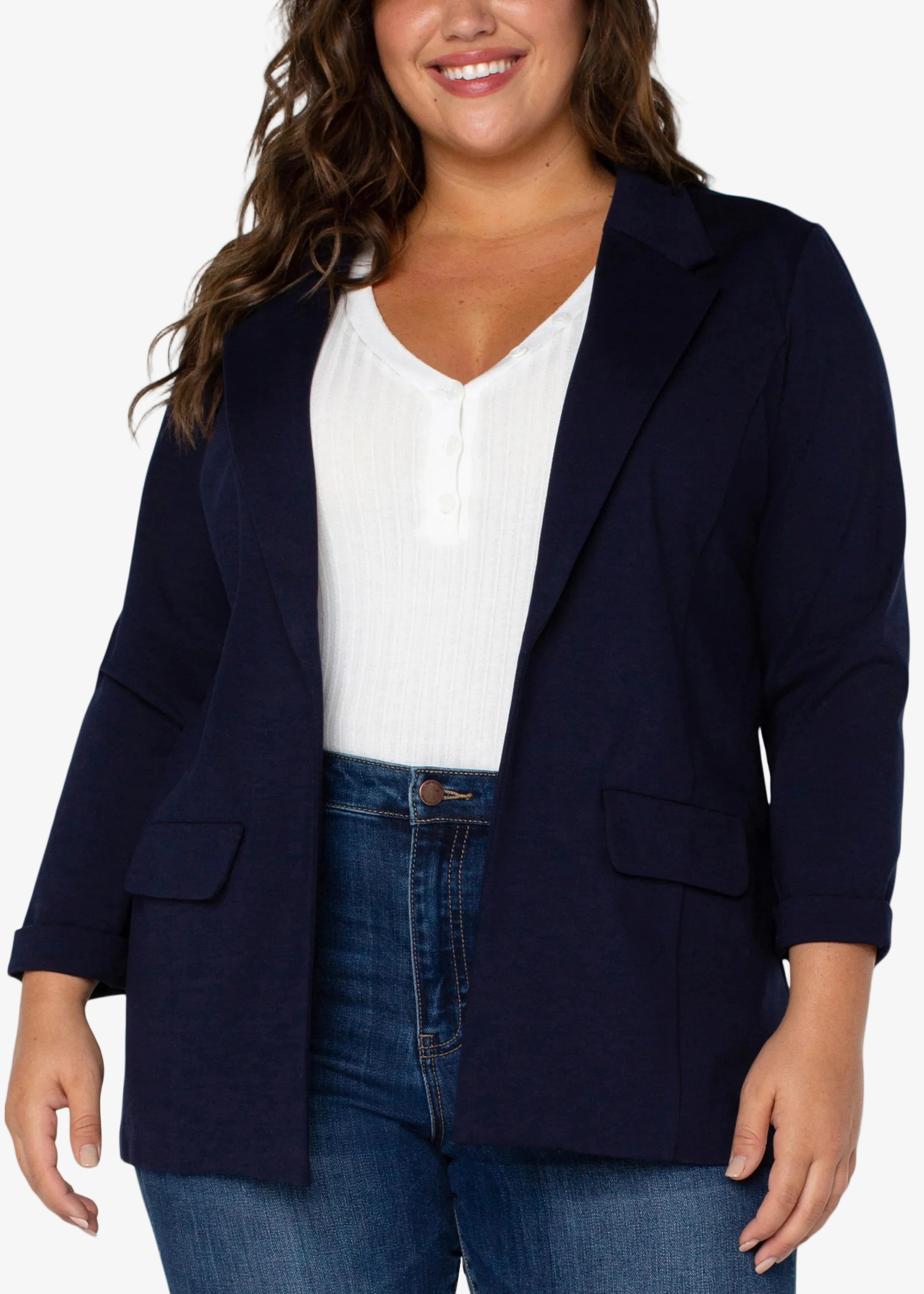 Woman wearing a navy blazer over a white top and blue jeans on a white background
