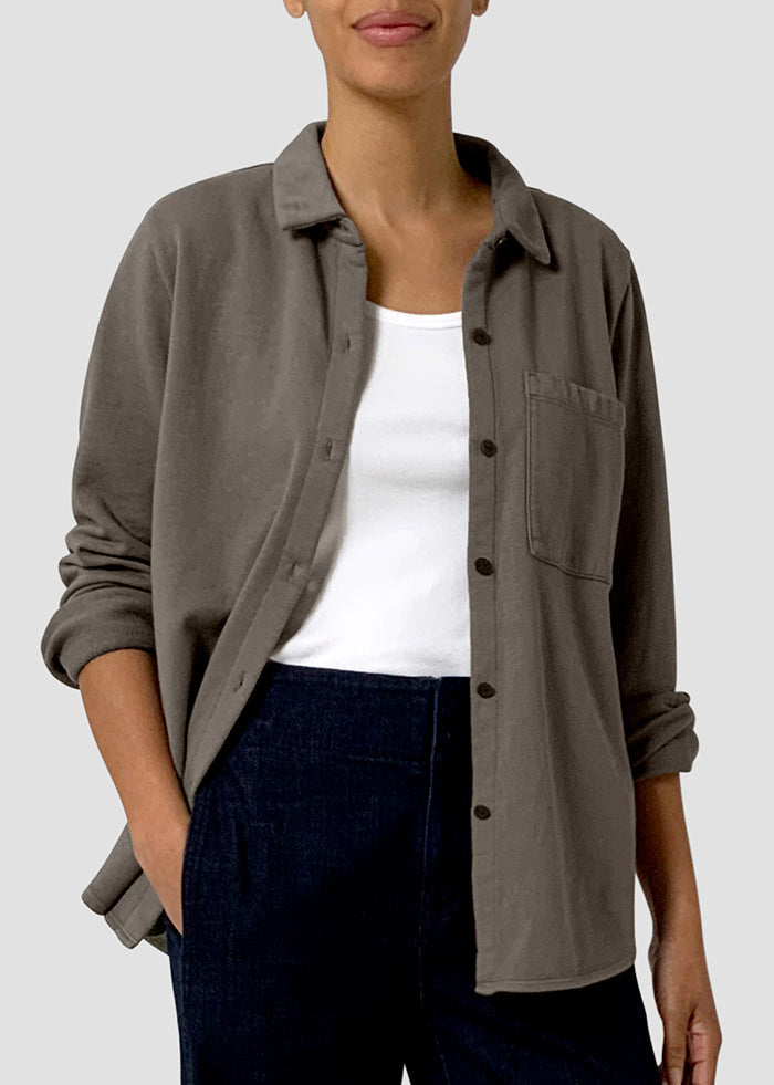 Person wearing a brown button-up shirt over a white top and dark pants on a light gray background