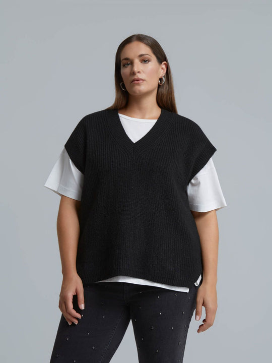 Black ribbed knit sweater vest with V-neck, worn over white t-shirt, front view
