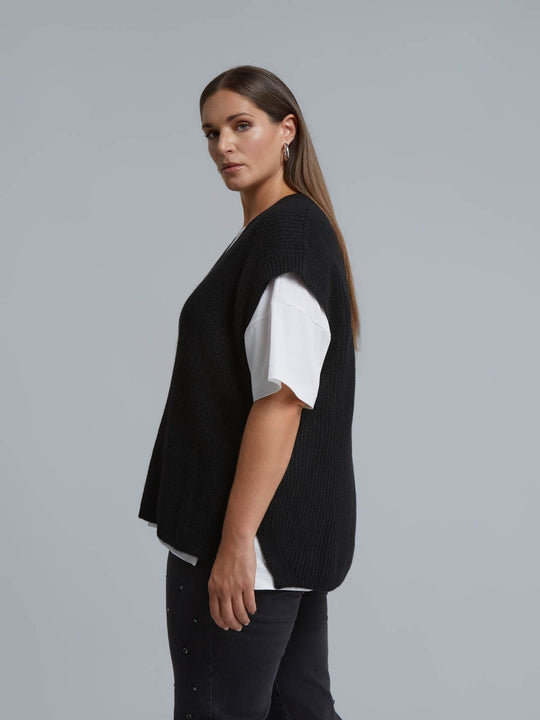 Black knit sweater vest with V-neck worn over white tee, side view on model