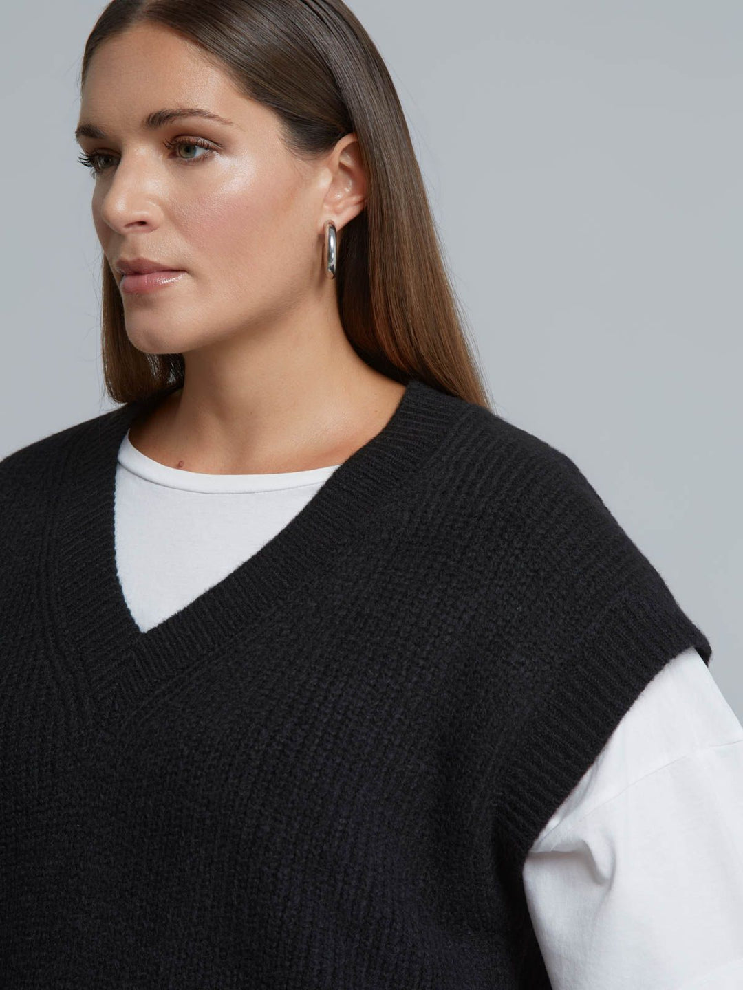 Black ribbed knit sweater vest with V-neck, layered over white long-sleeve top, close-up view