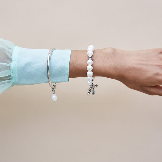 Silver pearl bracelet worn on wrist with small star-shaped charm dangle